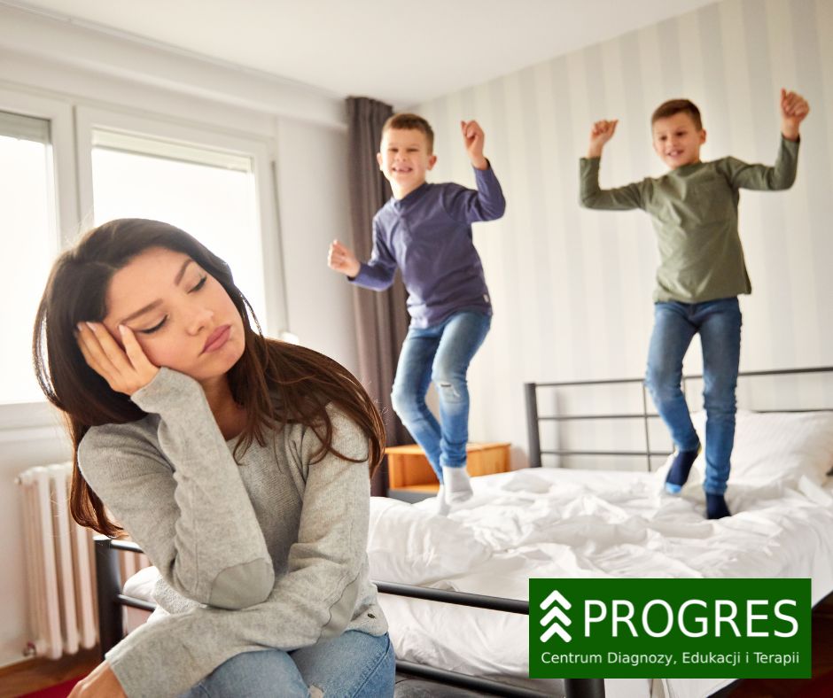 Zmęczona mama na pierwszym planie i dwoje energicznych dzieci skaczących po łóżku – ilustracja do tekstu o konsultacjach związanych z nadpobudliwością w Progres Pszczyna